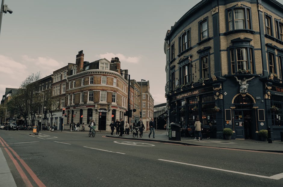 A street scene near Elephant and Castle showing a busy intersection with pedestrians walking on the pavement, some holding shopping bags, and cyclists riding through the crosswalk. On the corner, ther